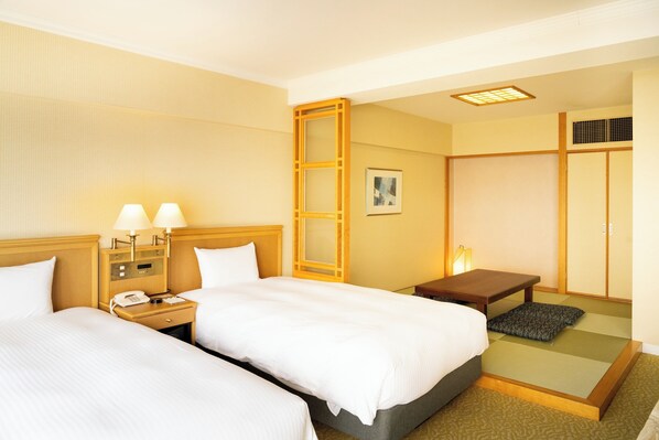 A hotel room with two beds, a nightstand with a phone, a small table, and a traditional Japanese sliding door.