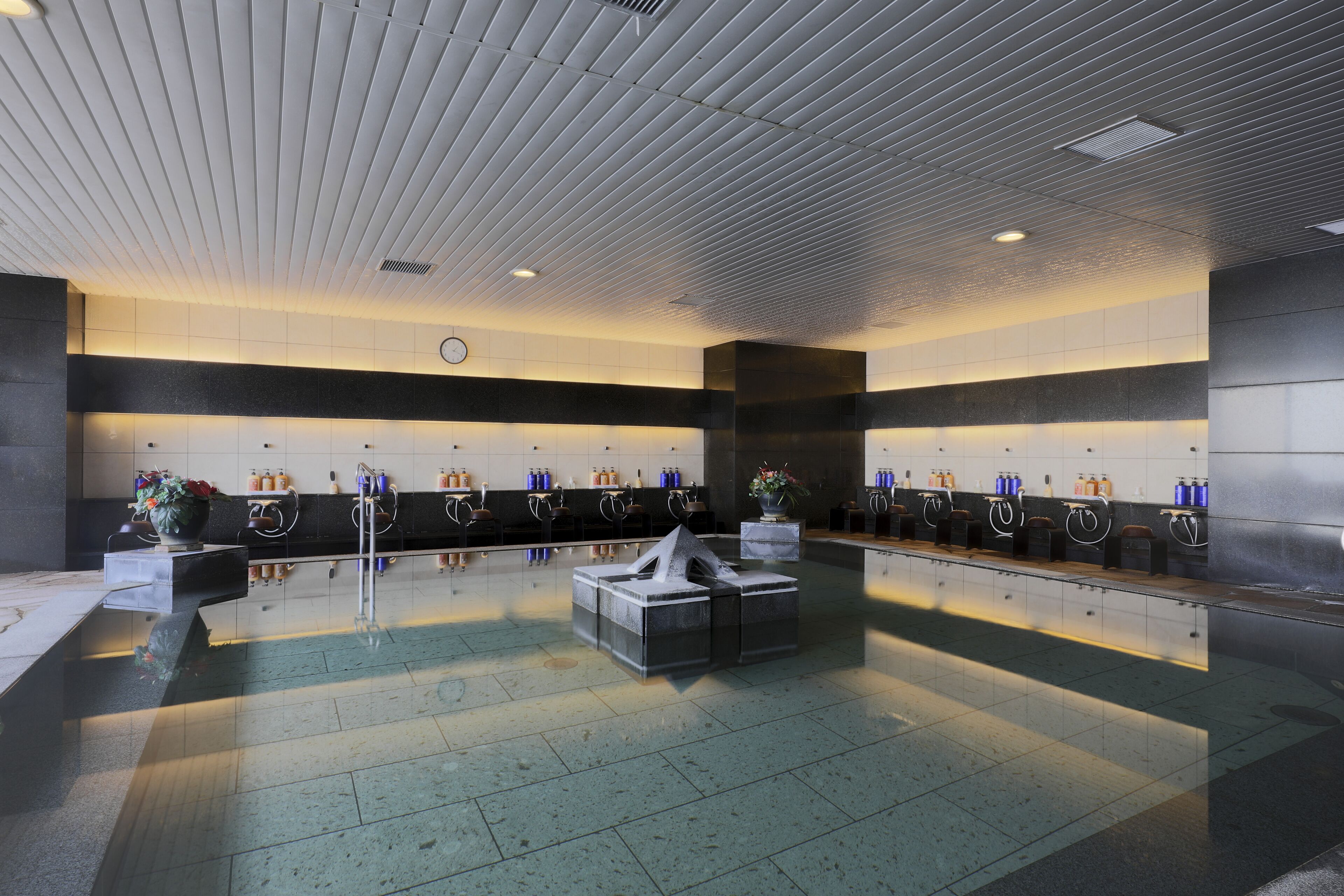 A modern bathroom with a central seating area, multiple sinks, and a decorative sculpture.
