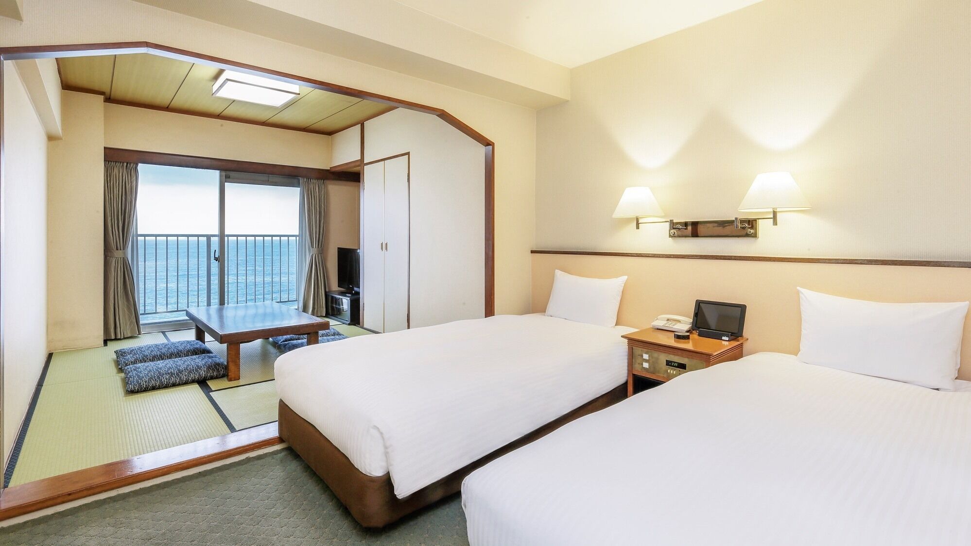 Une chambre d’hôtel avec deux lits, un bureau, une télévision et un balcon donnant sur la mer.