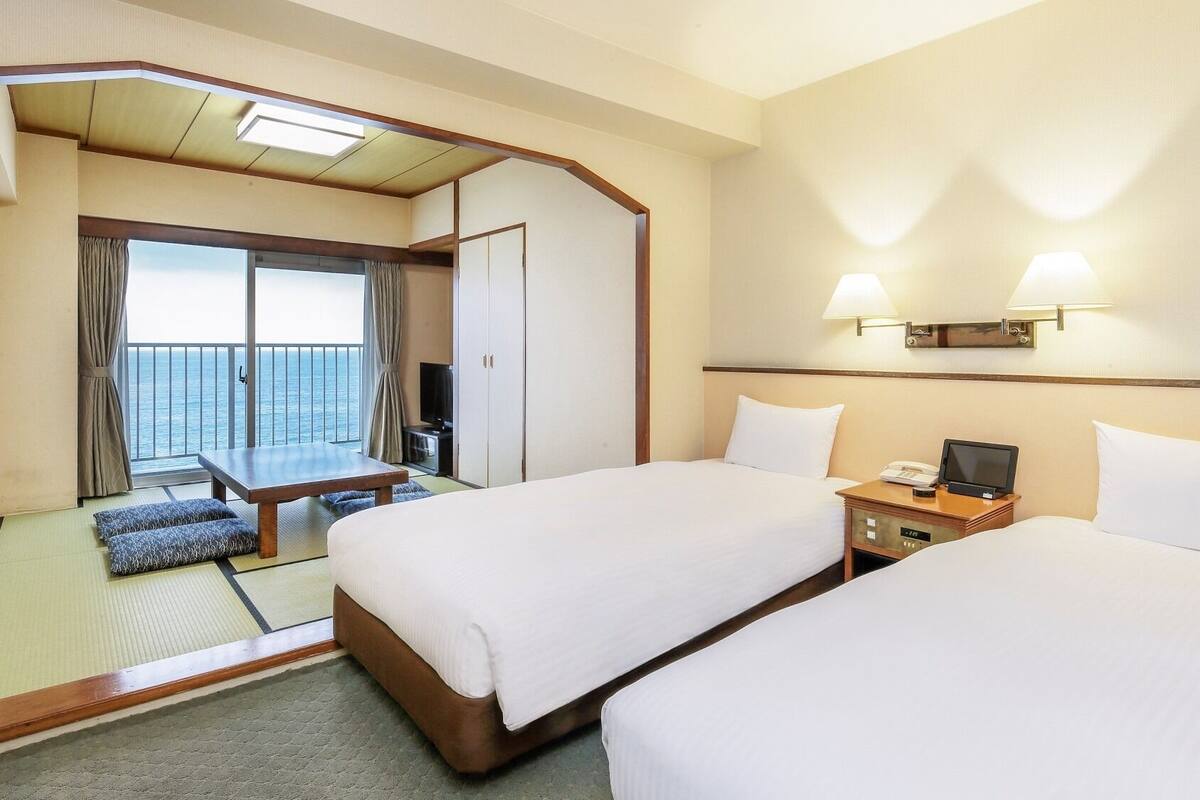 Habitación de hotel con dos camas, un escritorio, un televisor y un balcón con vista al mar.