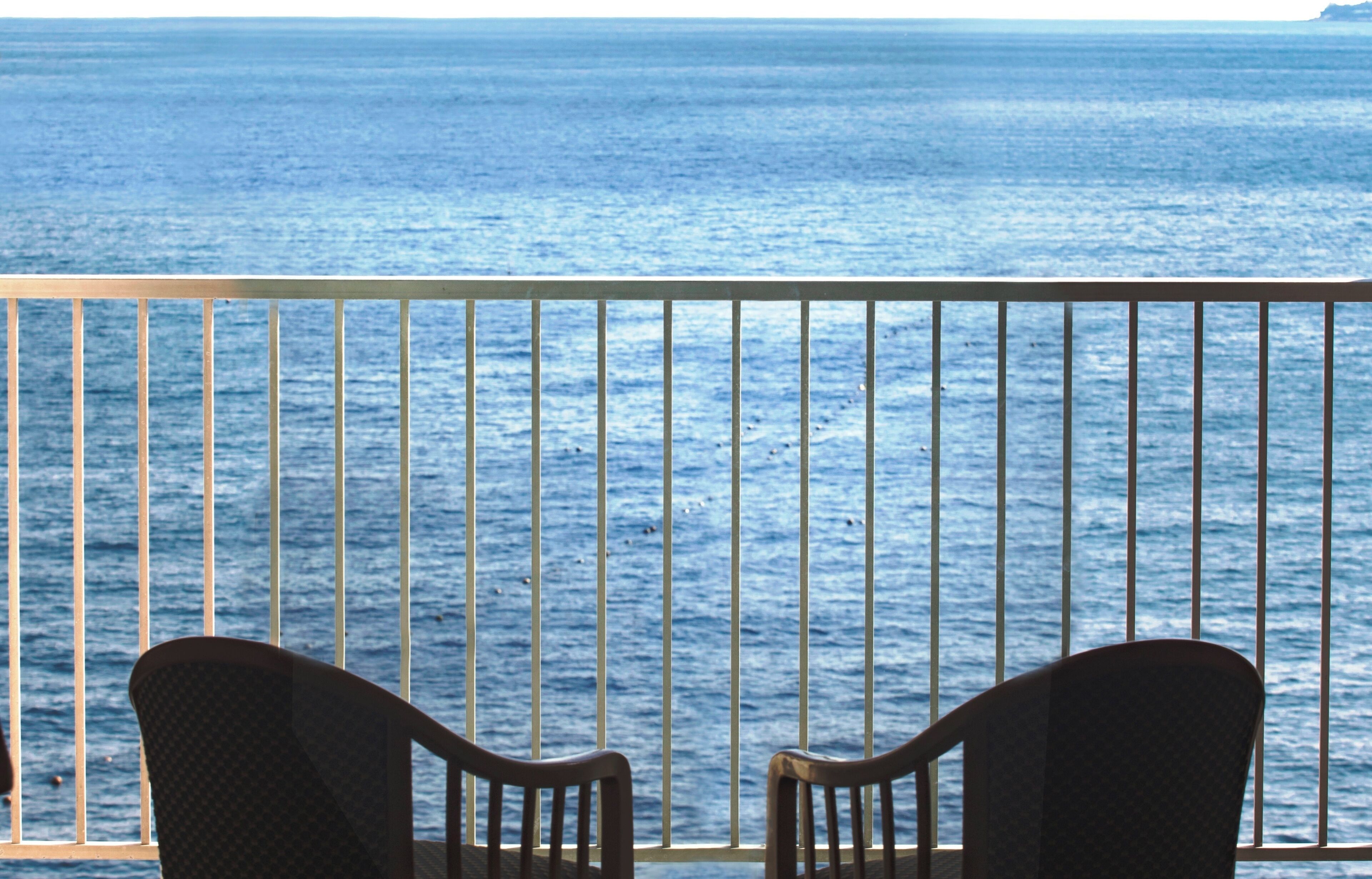 Een balkon met twee stoelen, gericht op een hekwerk met uitzicht op zee.