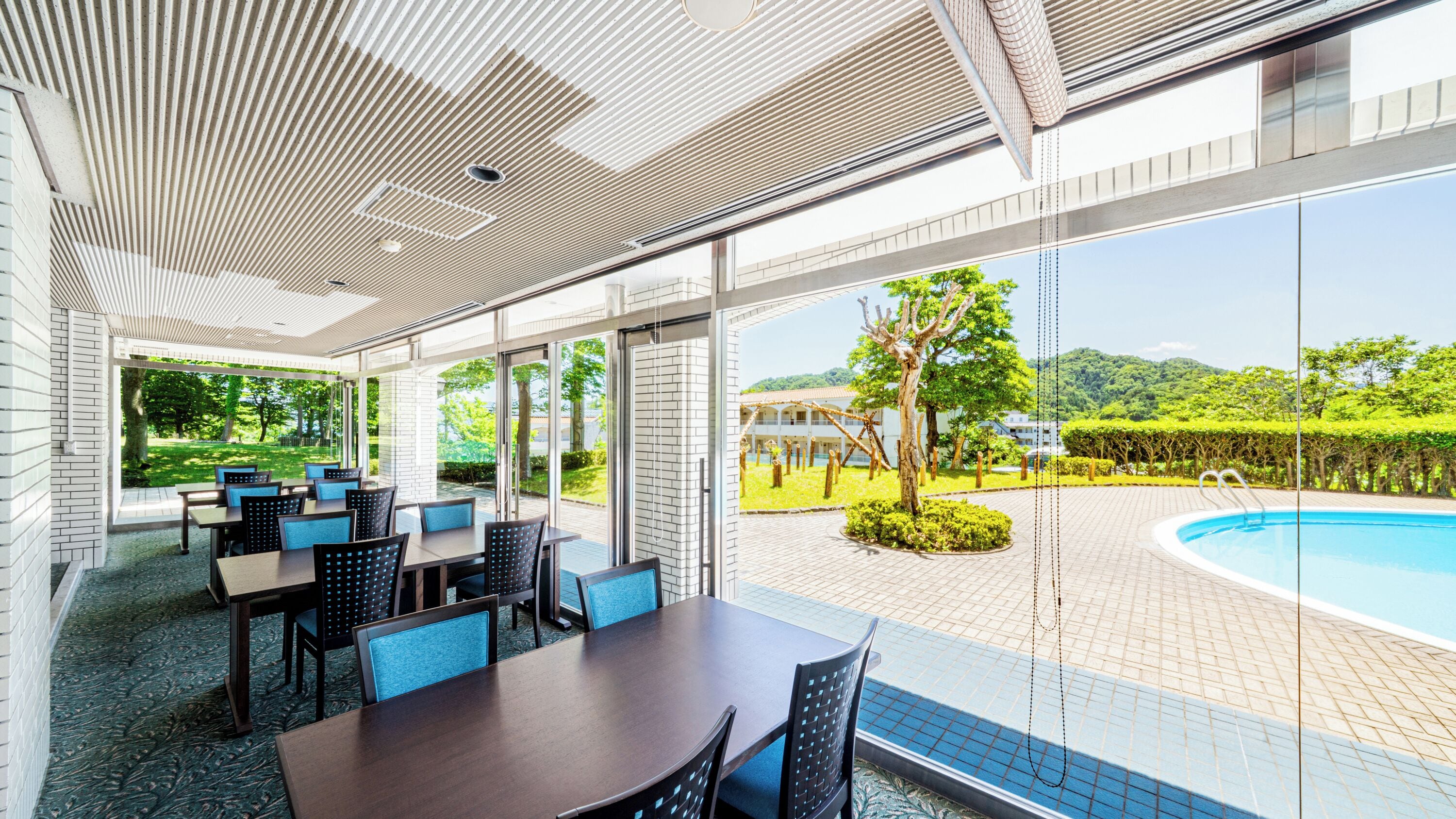 Un comedor interior moderno con vista a la piscina, que presenta una pared de ladrillo, puertas de vidrio y una zona de estar junto a la piscina.