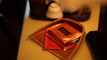 Una bandeja con una cesta trenzada marrón que contiene un sobre rojo y un pequeño objeto blanco, posiblemente un juego de té, sobre una mesa.