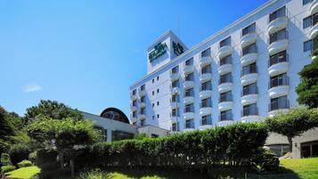 A multi-story hotel with balconies, a clear sky, and surrounding greenery.