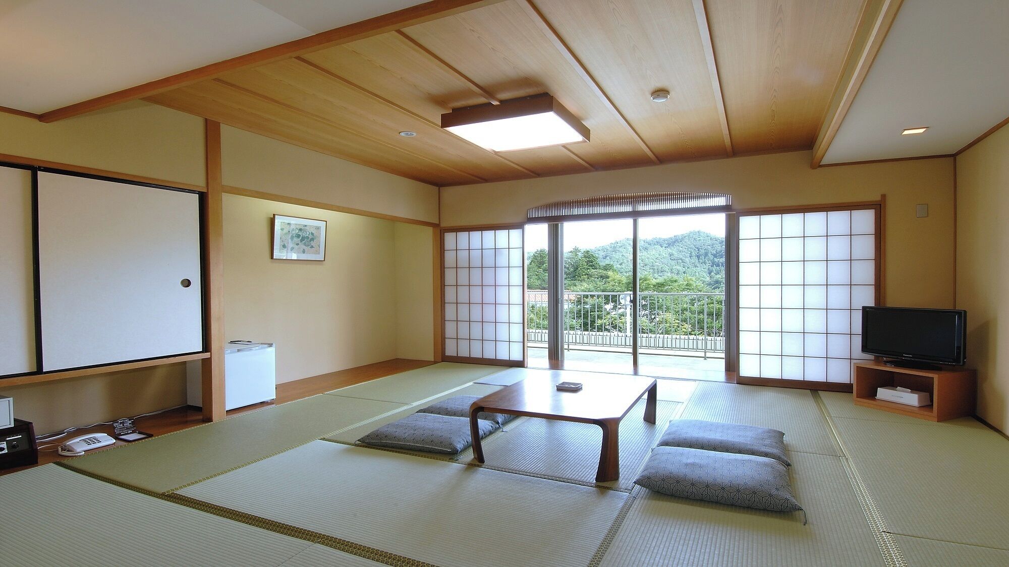 A traditional Japanese-style room with tatami flooring, a sliding door to a balcony, and a television on a wooden stand.
