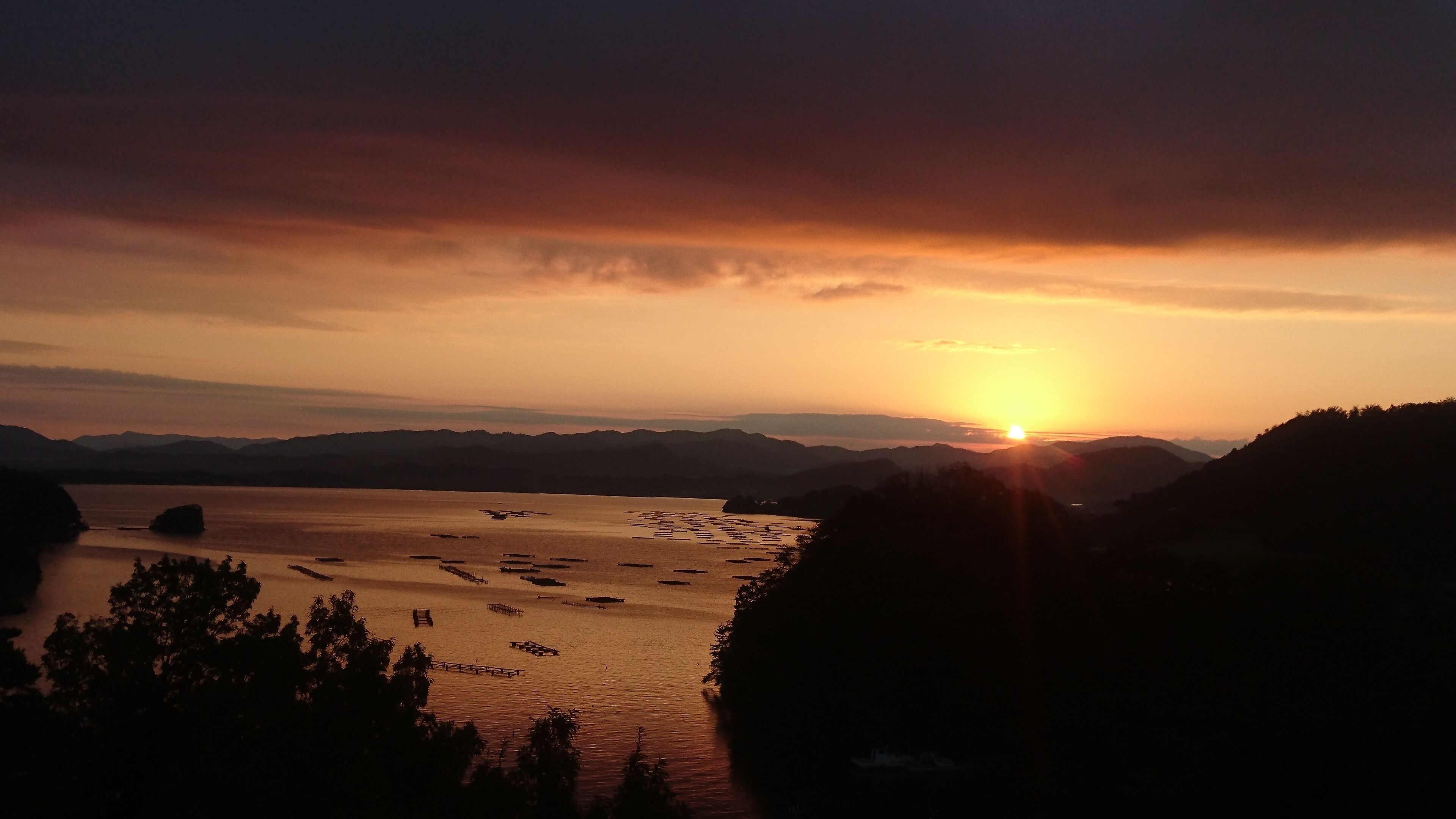 Ein Sonnenuntergang über einem Gewässer mit Bergen in der Ferne und einem klaren Himmel.