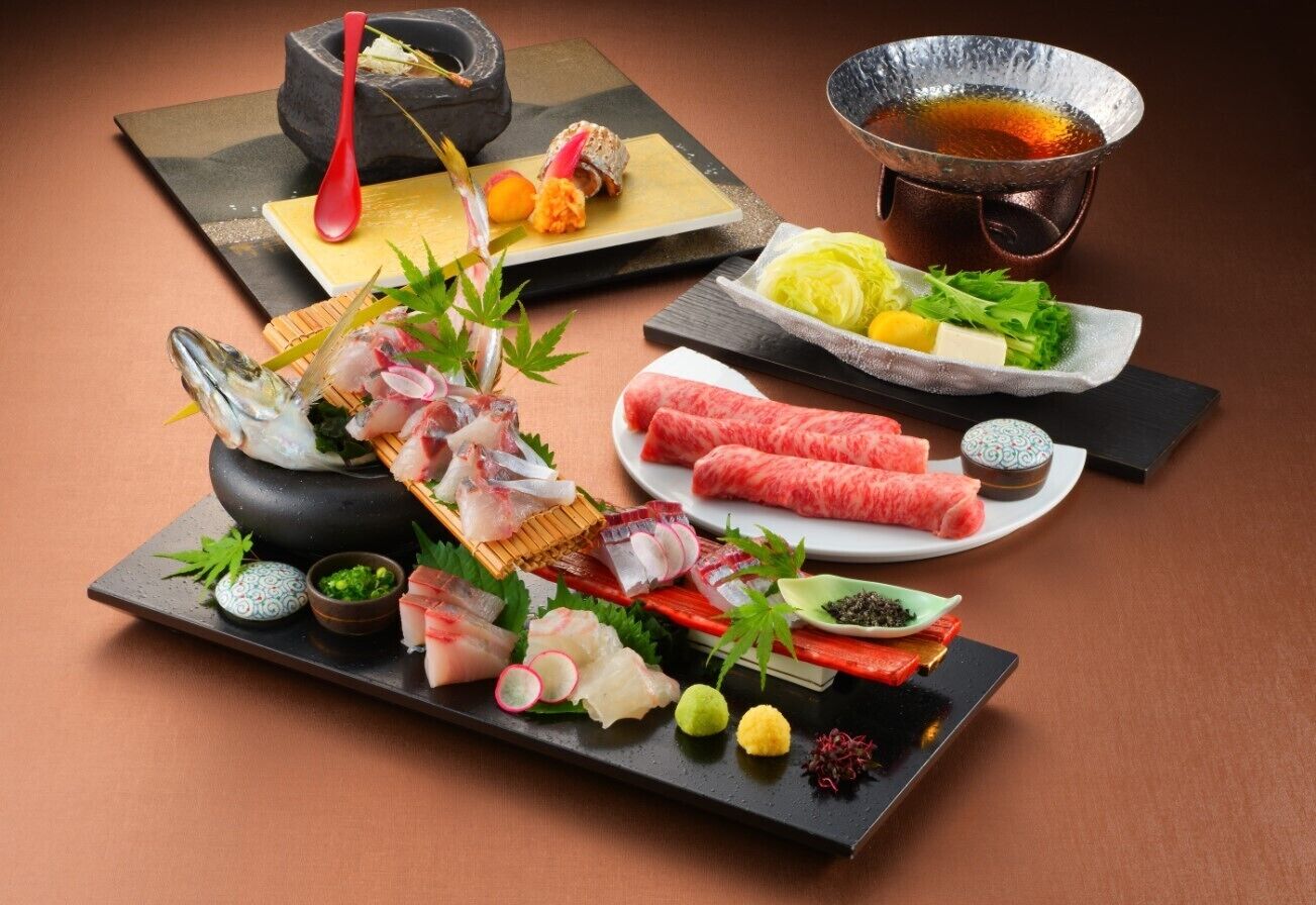 A variety of sushi and sashimi dishes, a hot pot, and a tea set on a table.