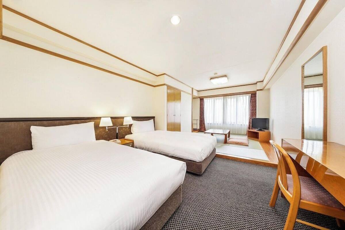 A hotel room with two beds, a desk, a chair, a television, and a large mirror.