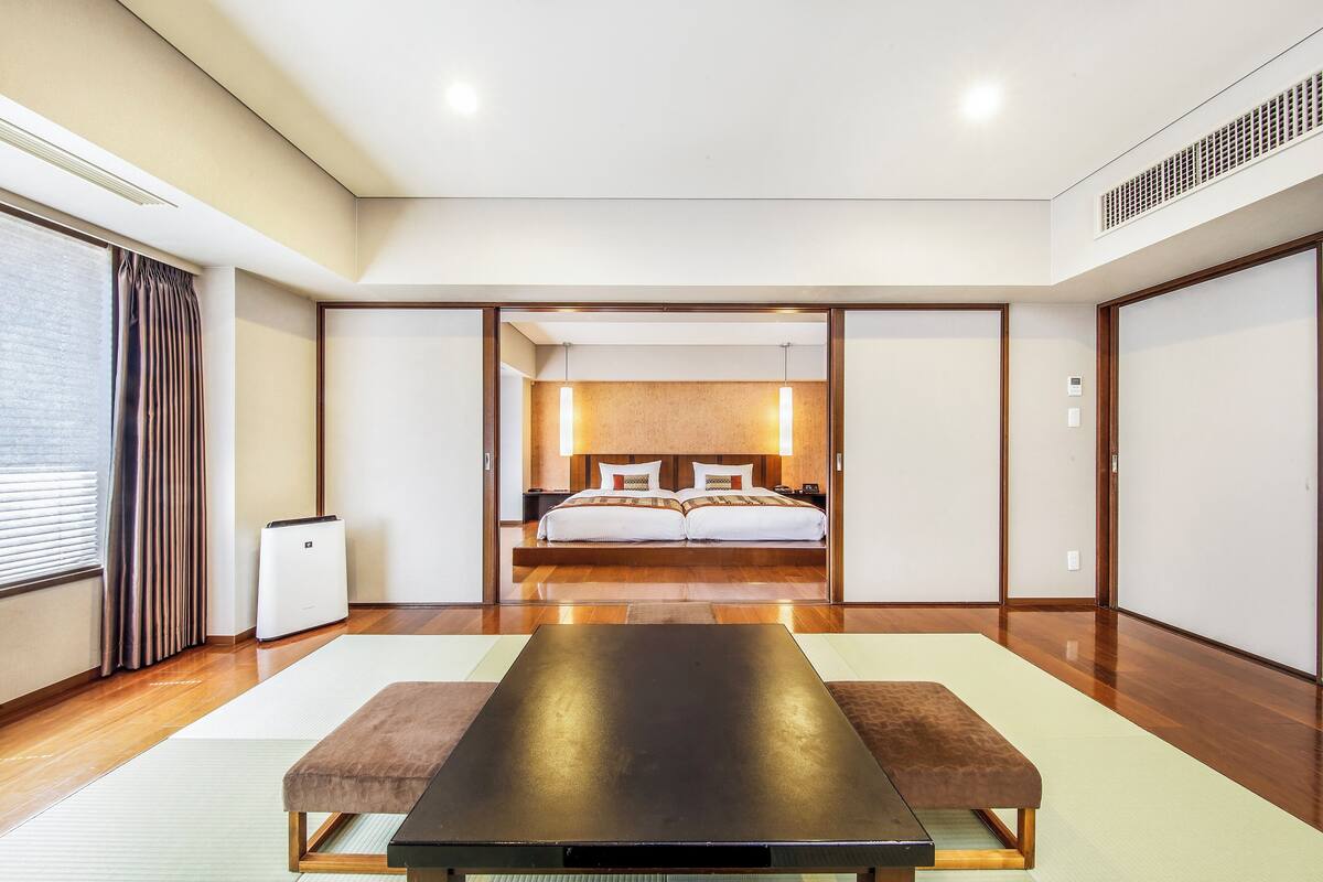 A hotel room with a large bed, a bedside table, a heater, and a view of the outside.