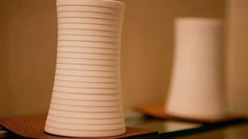 Un vase blanc orné de lignes horizontales, posé sur une surface réfléchissante.