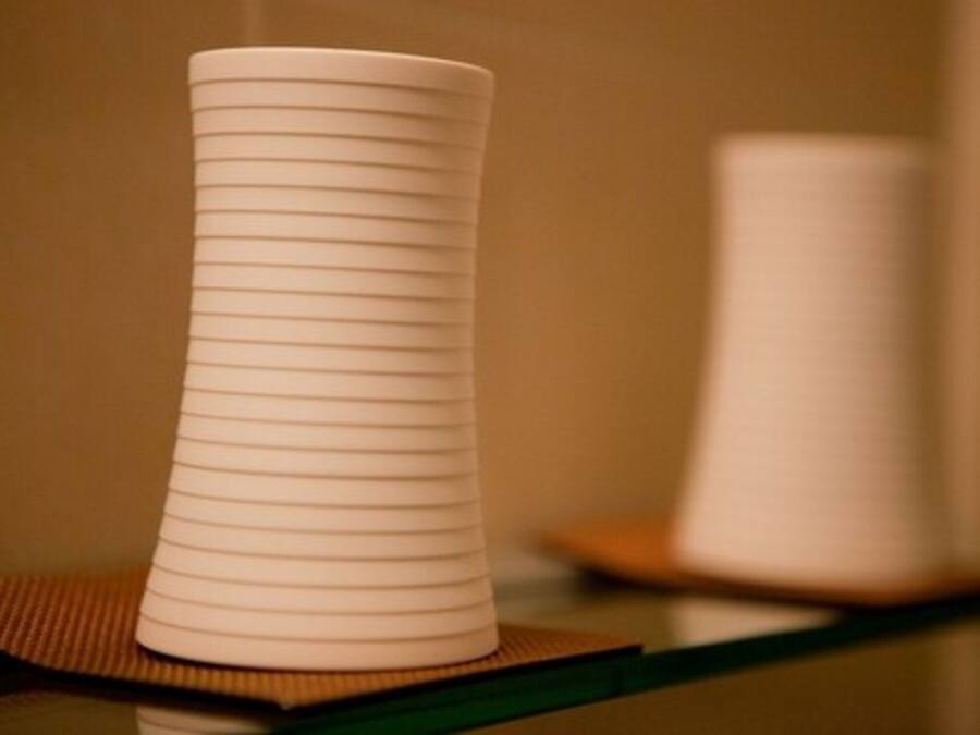 Un vase blanc orné de lignes horizontales, posé sur une surface réfléchissante.