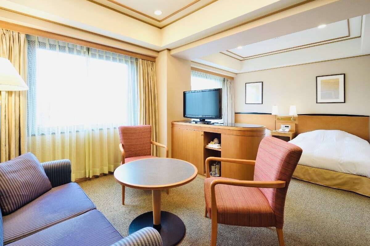 A hotel room with a bed, a TV, a desk, and two armchairs.