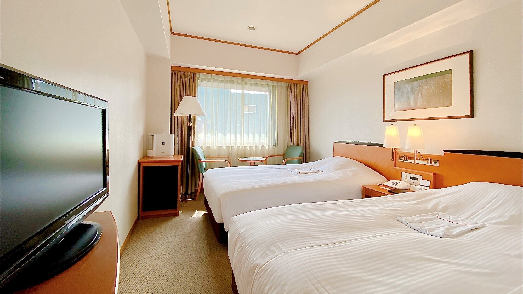 A hotel room with two beds, a TV, a desk with a lamp, a chair, and a painting on the wall.