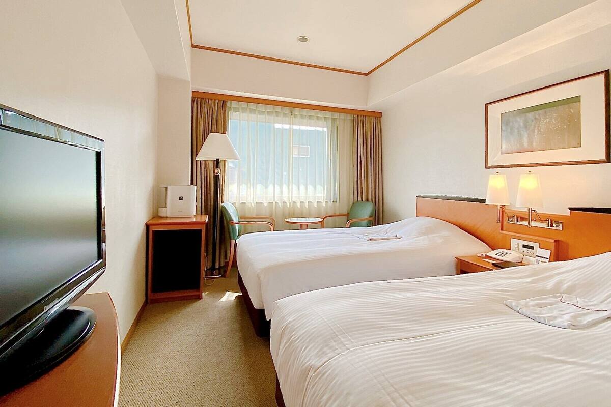 A hotel room with two beds, a TV, a desk with a lamp, a chair, and a painting on the wall.