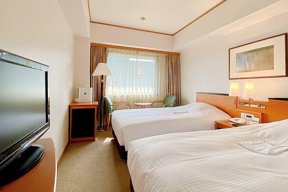 A hotel room with two beds, a TV, a desk with a lamp, a chair, and a painting on the wall.