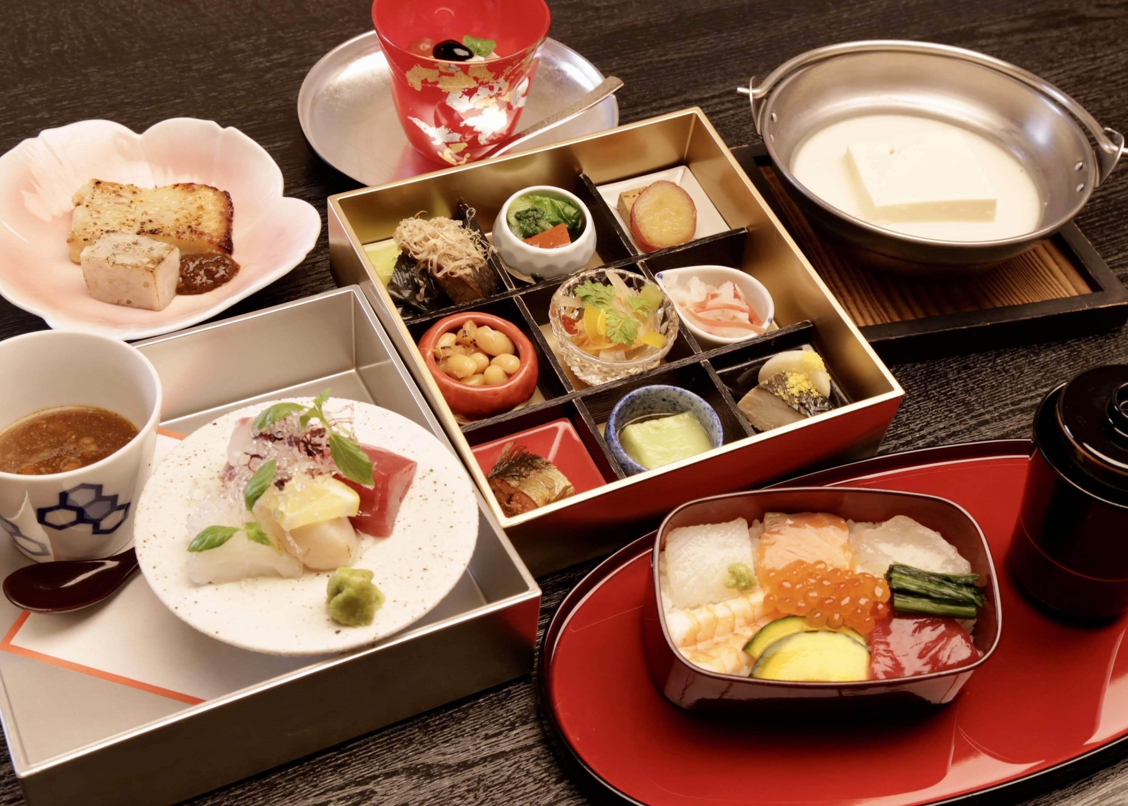 A variety of Japanese dishes arranged on a table, including sushi, sashimi, and other delicacies, served in traditional bento boxes and on plates.