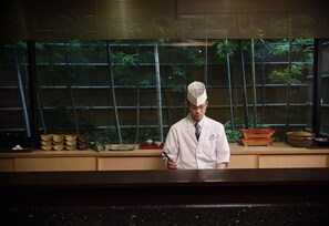 A person in a white lab coat standing in front of a window with bamboo plants. - Sun Members Kyoto Saga (Kyoto)