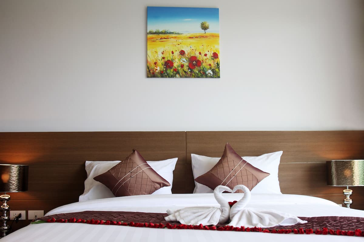A hotel room with a wooden headboard, white bedding, and a painting of a field with a tree.