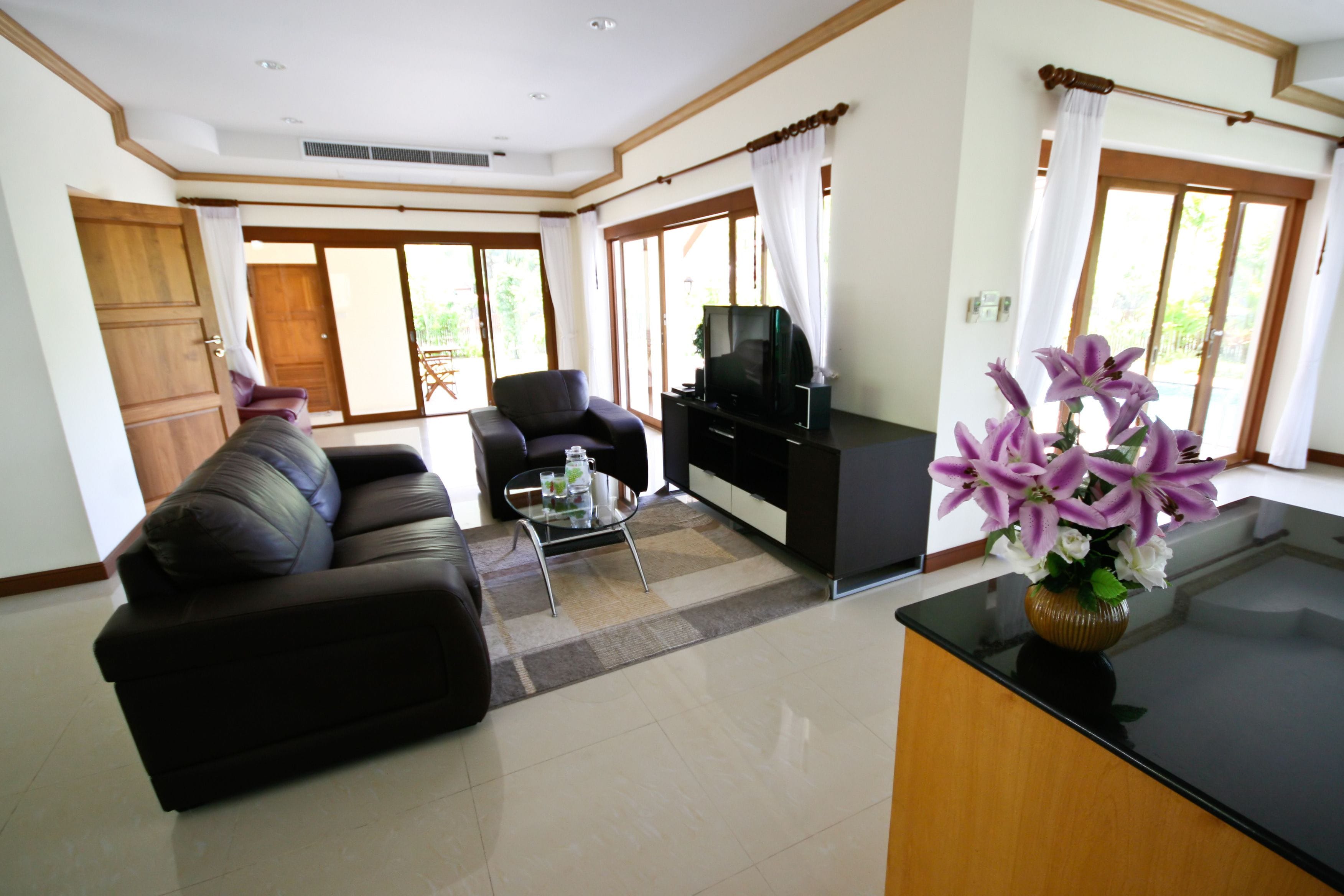 A spacious living room with a sofa, a coffee table, a TV, and a vase of flowers.