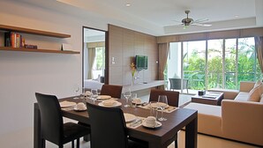 A modern dining area with a wooden table set for four, a sofa, and a TV mounted on the wall. - Bangtao Tropical Residence Resort & Spa (Choeng Thale)