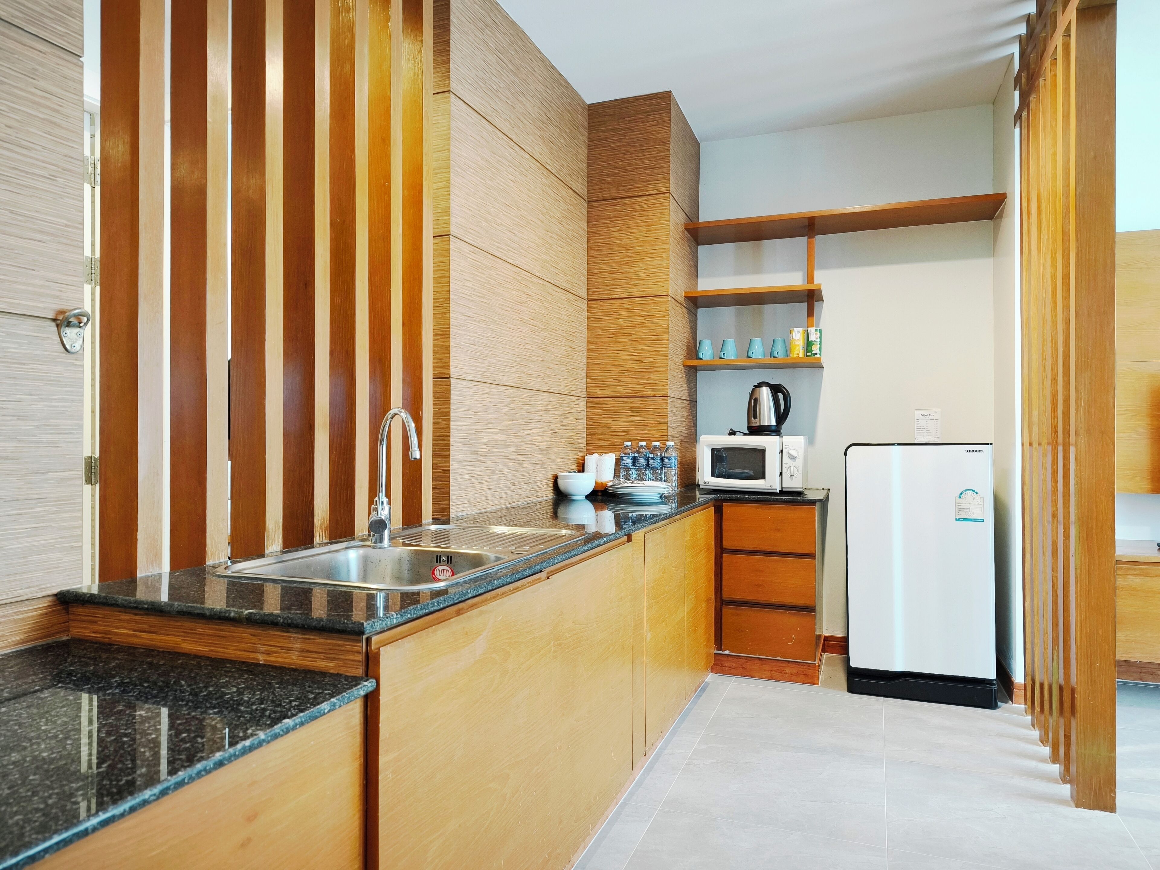 A modern kitchen with a granite countertop, stainless steel sink, wooden cabinets, a microwave, and a refrigerator.