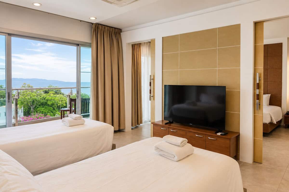Habitación de hotel con dos camas, televisión y balcón con vistas.