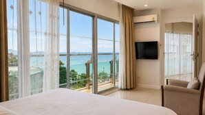 A hotel room with a large bed, a TV, a chair, and a balcony with a view of the sea. - Royal Beach View Suites (Pattaya)