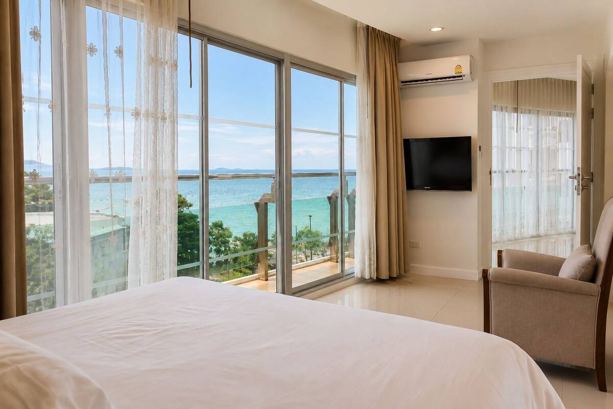 Habitación de hotel con una cama grande, televisión, silla y balcón con vista al mar.