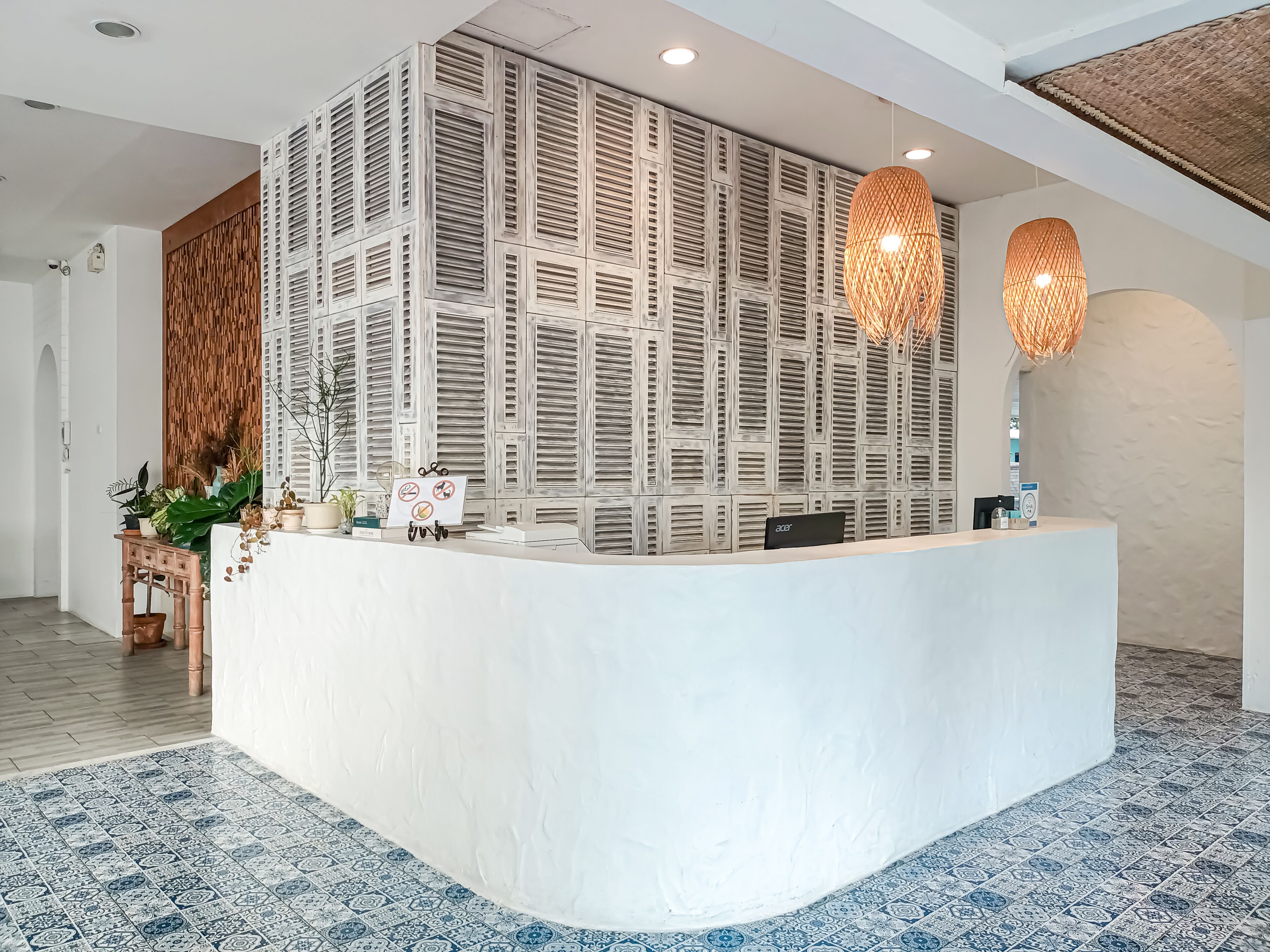 A reception area with a modern design, featuring a white reception desk, a decorative wall with a pattern, and two hanging lamps.