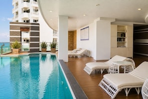 Un espace aménagé au bord de la piscine, avec des chaises longues, une petite table et une bibliothèque.