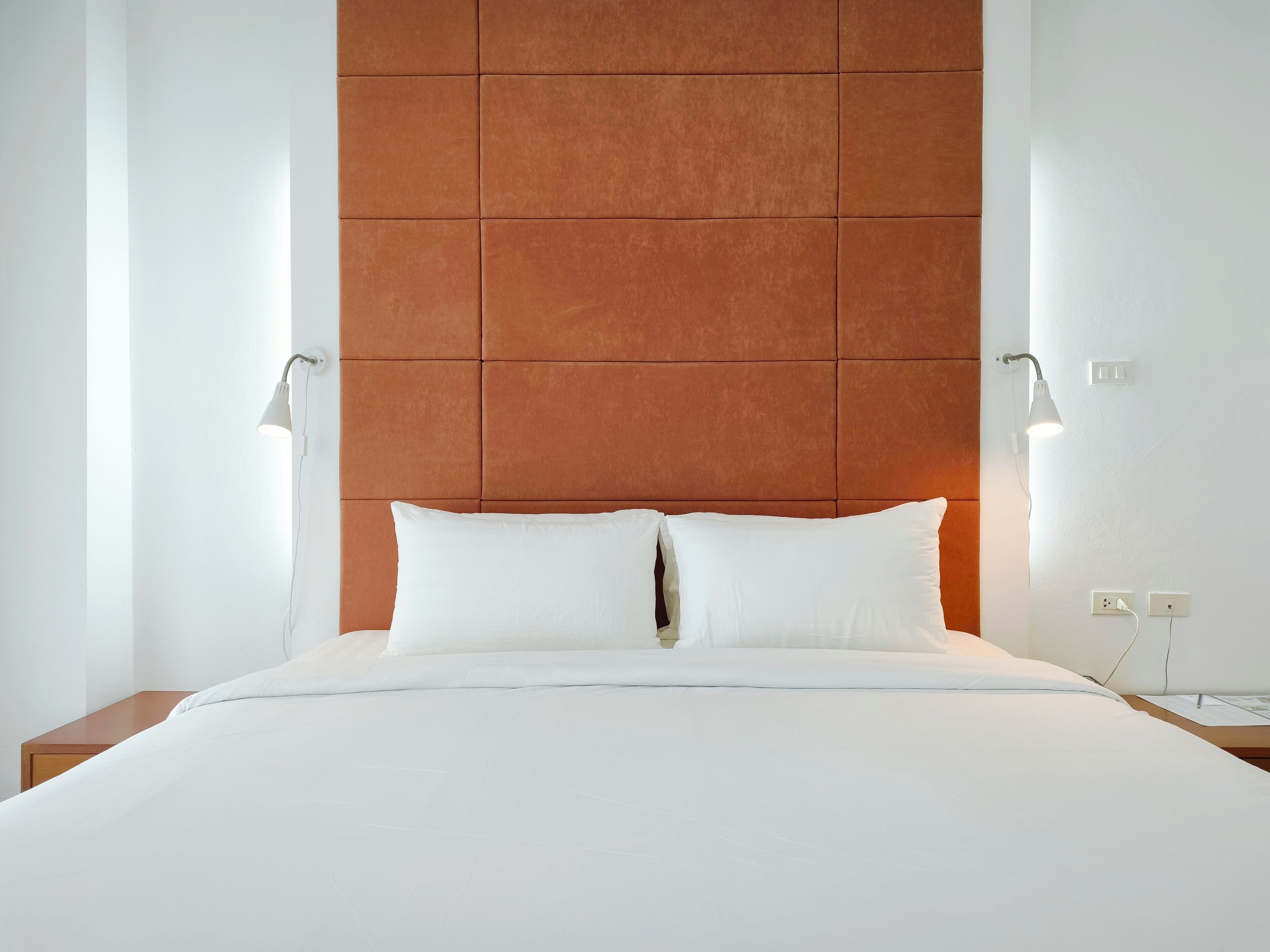 Una habitación de hotel con una cama grande, dos lámparas de noche y un cabecero moderno.