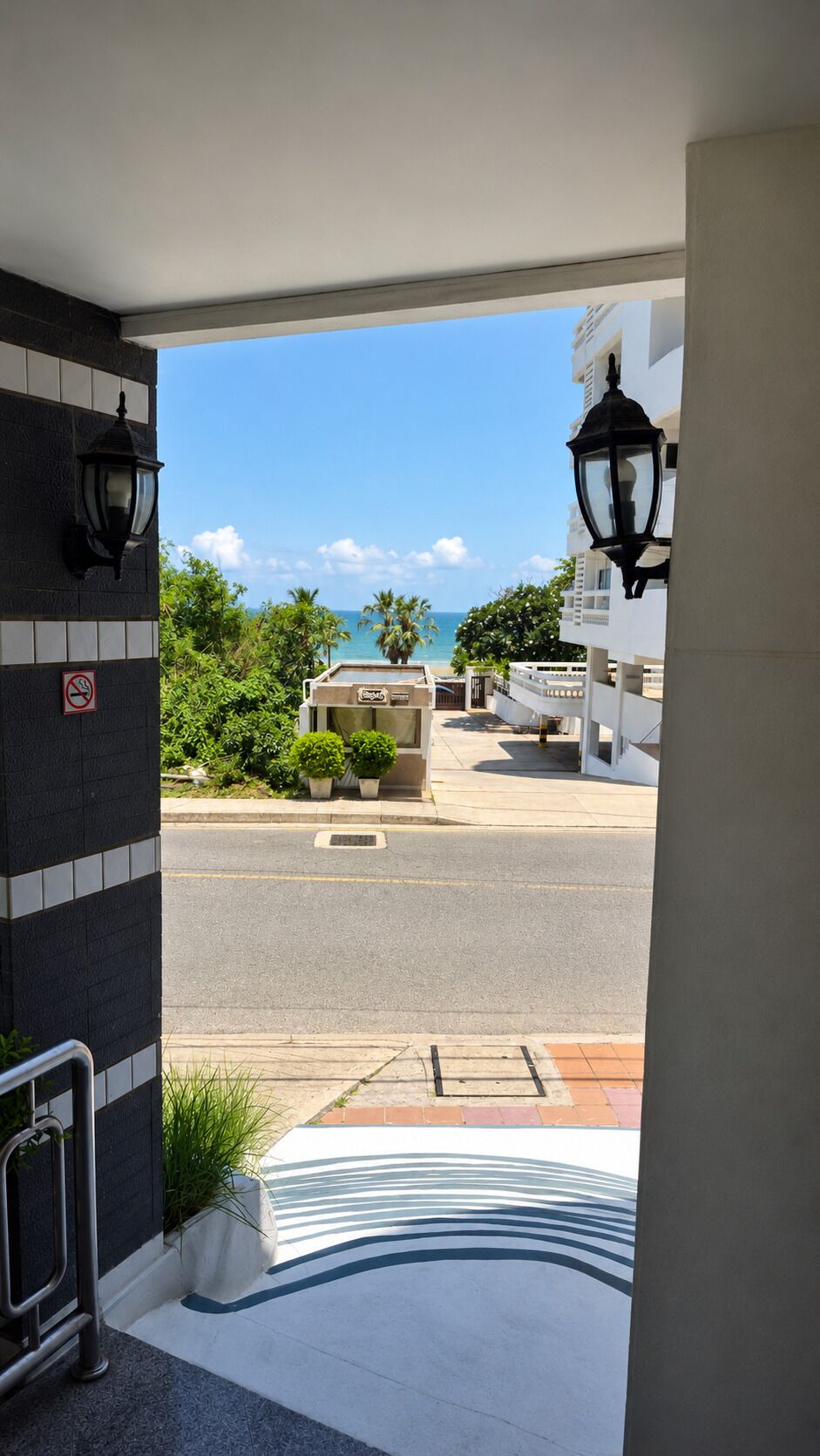 A hotel entrance with a view of the street, a no-smoking sign, and a lamp post.