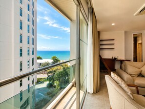 A modern living room with a balcony overlooking a building and a clear view of the ocean. - Royal Beach View Suites (Pattaya)