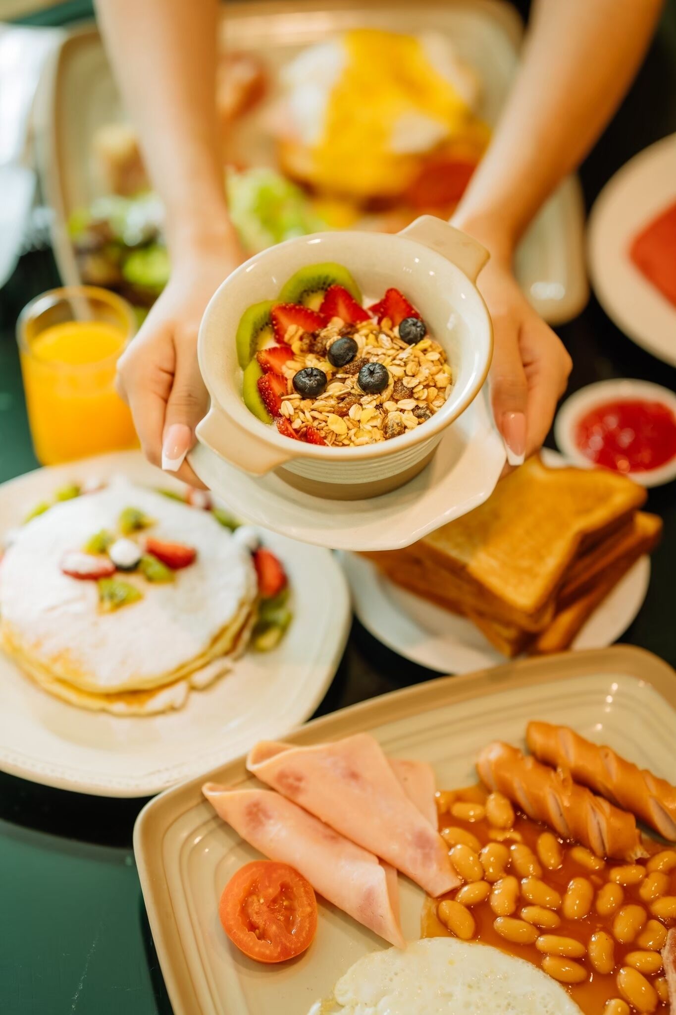 Bandeja de desayuno con panqueques, tostadas, frijoles y un tazón de cereal con frutas y granola.
