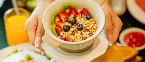 Bandeja de desayuno con panqueques, tostadas, frijoles y un tazón de cereal con frutas y granola.
