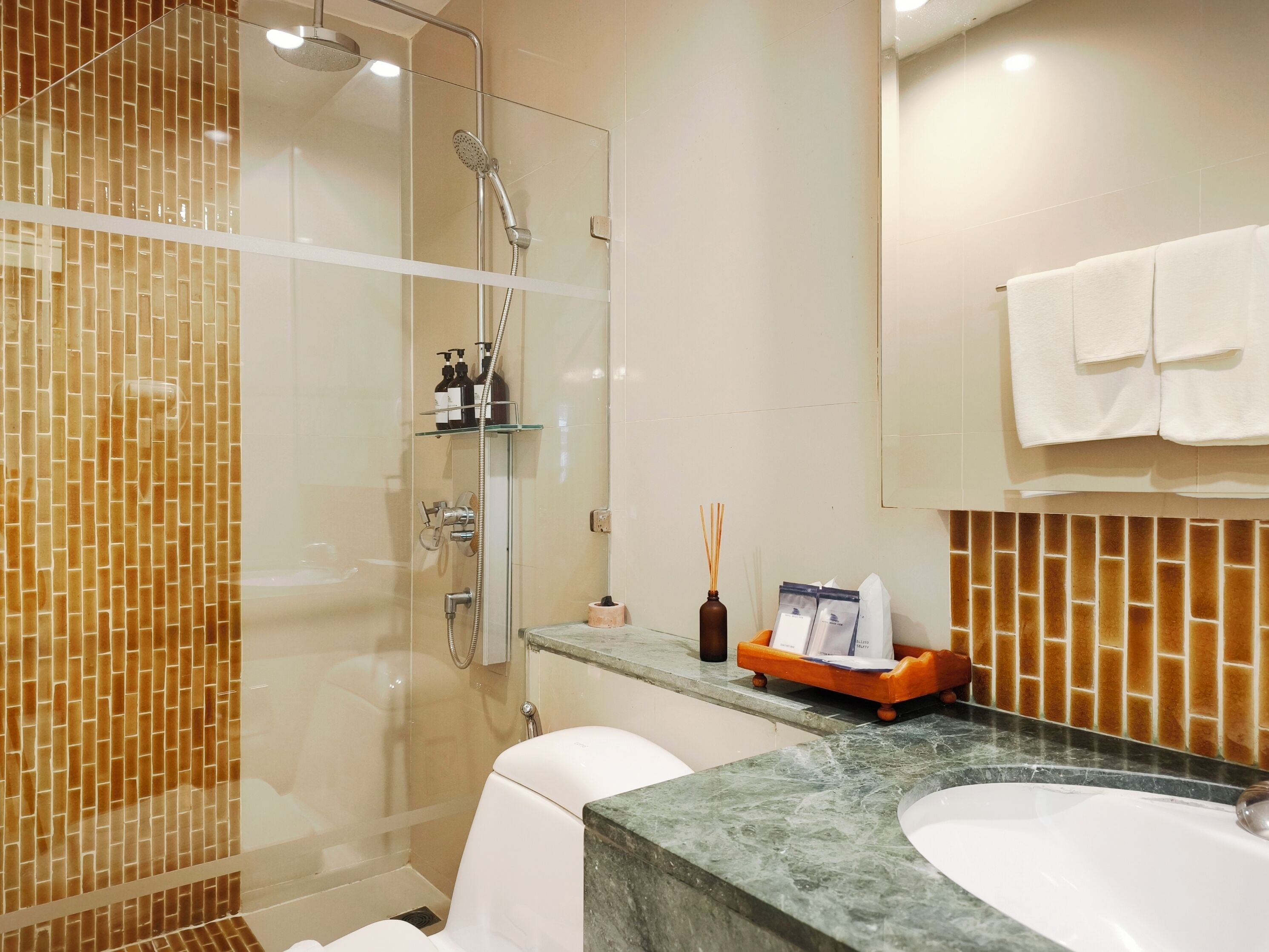 A modern bathroom with a glass-enclosed shower, a white toilet, a sink with a marble countertop, and a mirror above the sink.