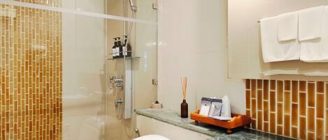 A modern bathroom with a glass-enclosed shower, a white toilet, a sink with a marble countertop, and a mirror above the sink.