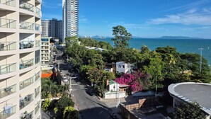 A high-rise building with multiple balconies, a clear view of the sea, and a mix of greenery and urban structures. - Royal Beach View Suites (Pattaya)