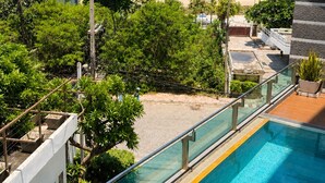 A swimming pool with a glass barrier, a view of the beach, and surrounding greenery. - Royal Beach View Suites (Pattaya)