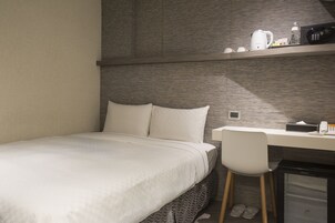 Een moderne hotelkamer met een bed, bureau, stoel en een kleine kitchenette.