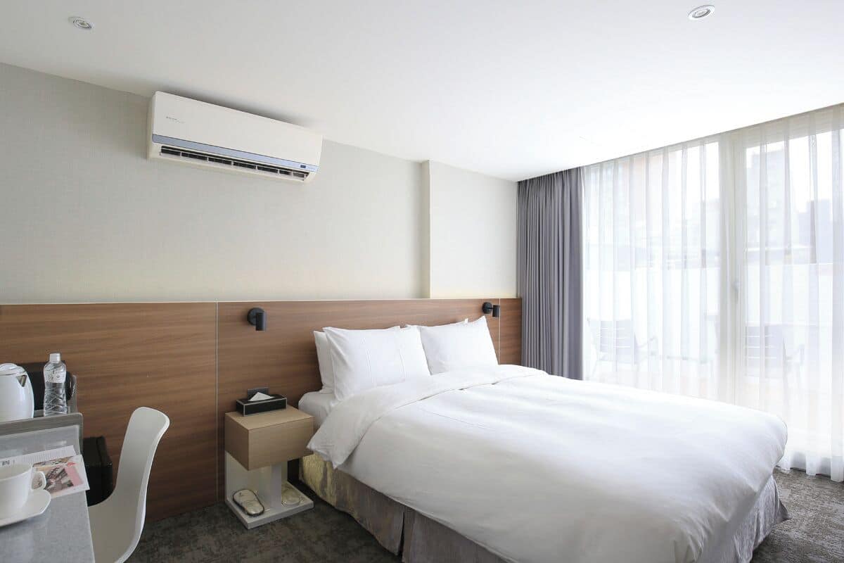 Ein Hotelzimmer mit Bett, Nachttisch, Sessel und Klimaanlage.