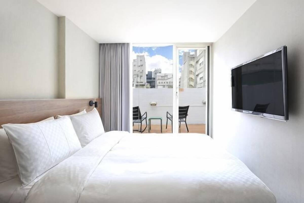 Ein Hotelzimmer mit Bett, Fernseher, Balkon mit Tisch und Stühlen und Blick auf die Stadt.