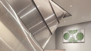 Een moderne wachtruimte met grijs gestoffeerde stoelen, een kamerbreed tapijt en een kunstwerk aan de muur.