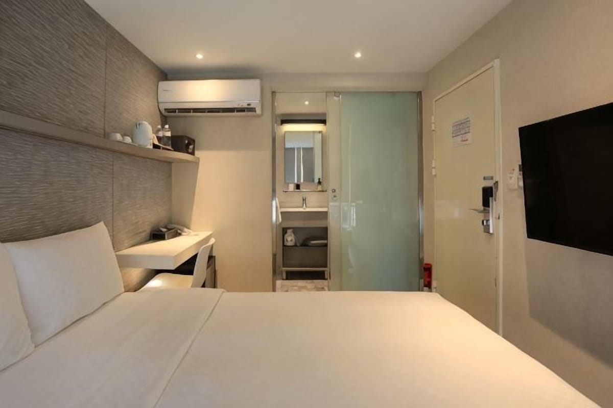 A hotel room with a bed, a desk, a mirror, a TV, and a wardrobe.
