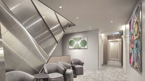 Een moderne hal met een geometrisch wandontwerp, een behang met patroon en een zithoek met grijs gestoffeerde stoelen en poefjes.
