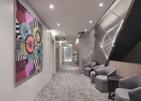 Un pasillo moderno con decoración mural estampada, piso alfombrado y rincones de estar con otomanas y sillones.