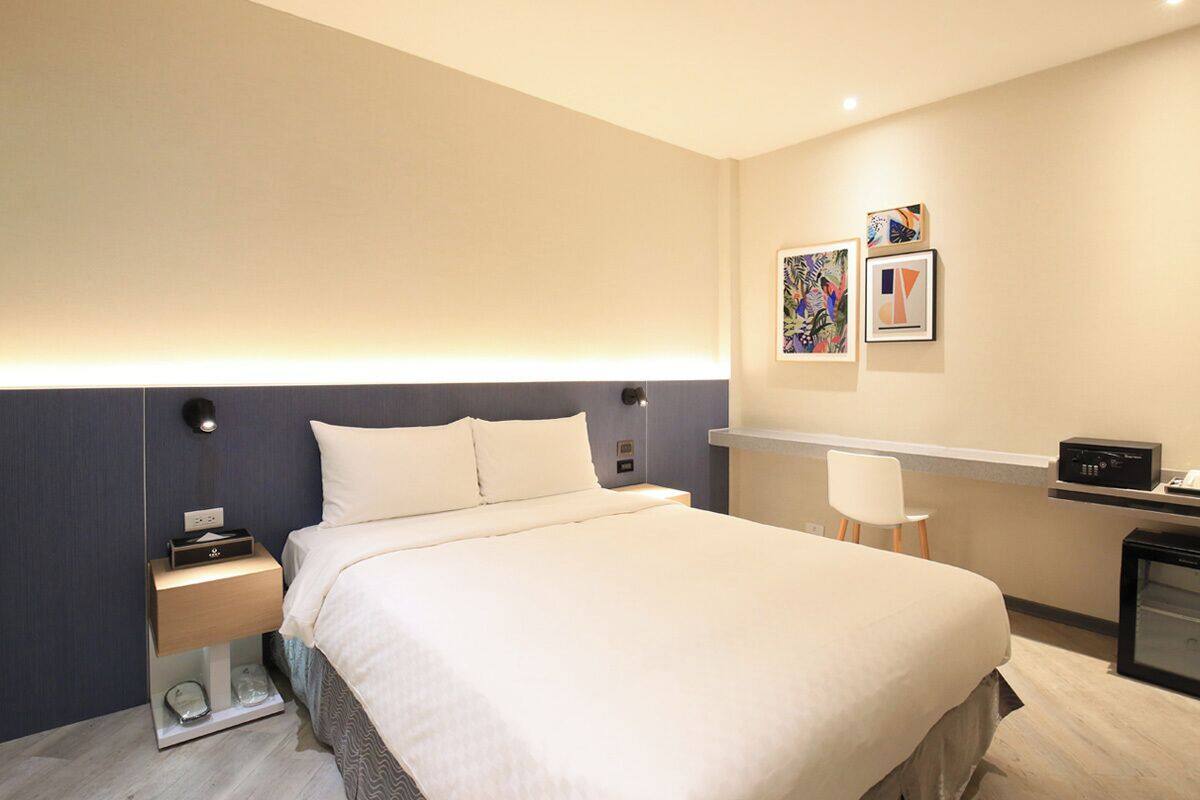 Ein modernes Hotelzimmer mit einem großen Bett, Nachttischen, einem Schreibtisch mit Stuhl und einem Kunstwerk an der Wand.