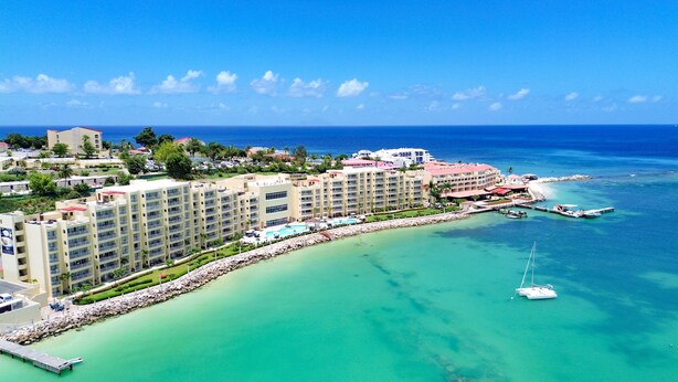 Un complejo turístico con varias edificaciones de hotel, un puerto deportivo y un océano azul cristalino.