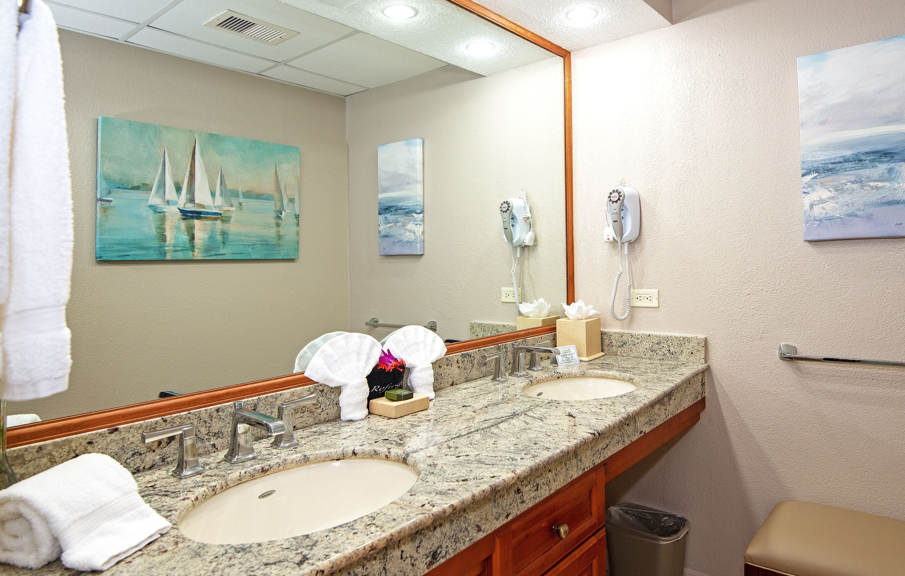 A hotel bathroom with two sinks, a large mirror, and artwork on the walls.