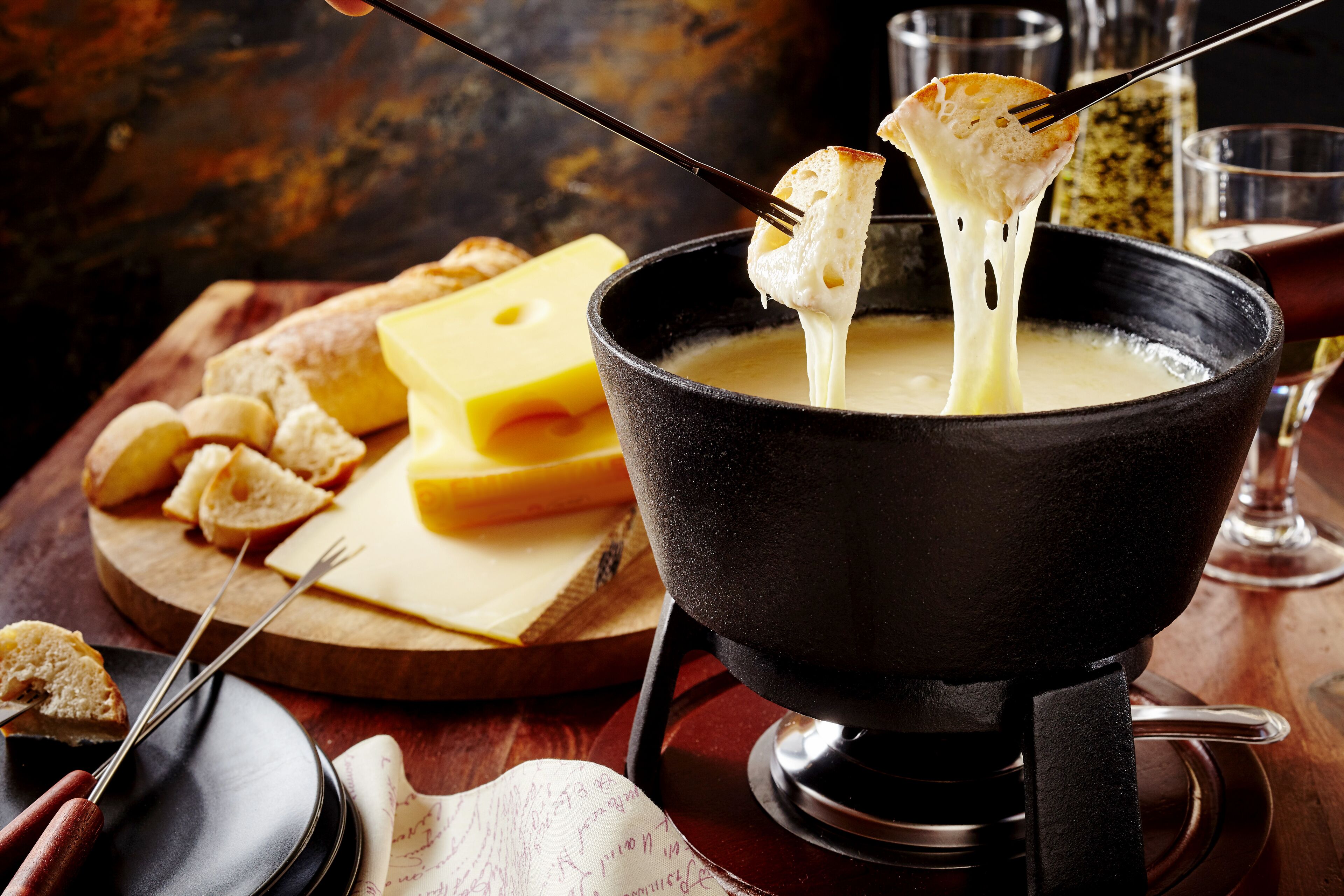 Ein Käsefondue-Set mit Käse und Brot auf einer Holzplatte.